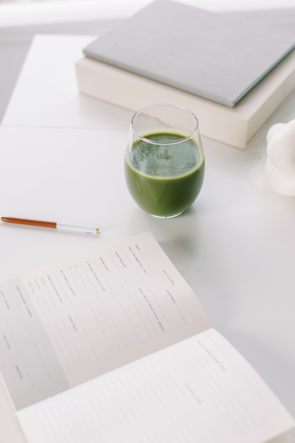 A glass of green juice, a pen, and an open planner on a clean, white table representing holistic wellness at Liv Med Spa in Sioux Falls